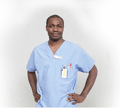 A front-facing, upper body shot of a doctor in scrubs with his hands on his hips.